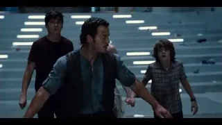 four people walking in dimly lit room with stairs — Jurassic World